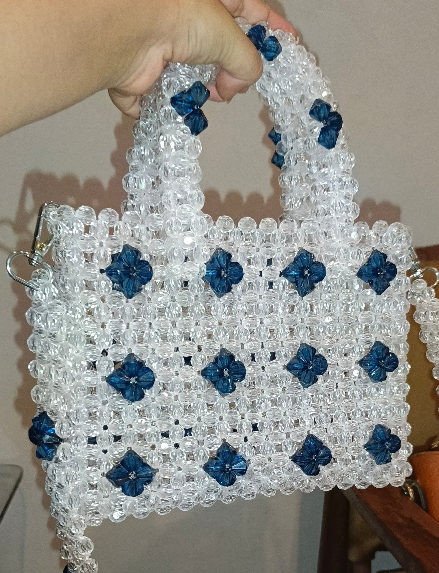 Handmade beaded bag with blue flowers held by a person indoors.