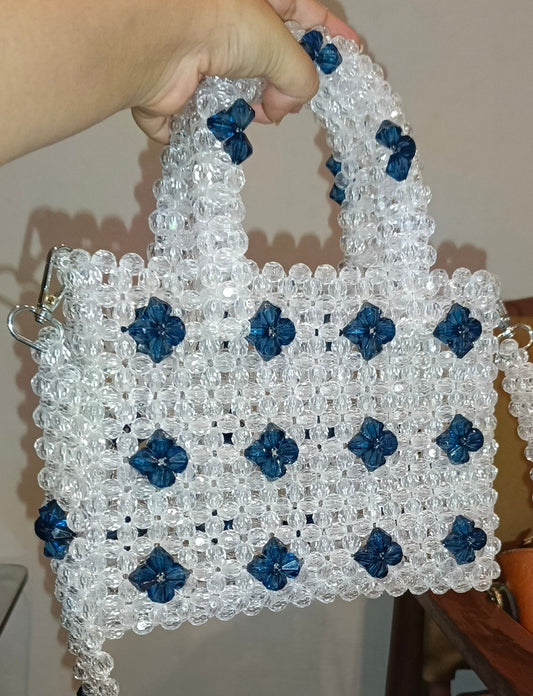 Handmade beaded bag with blue flowers held by a person indoors.